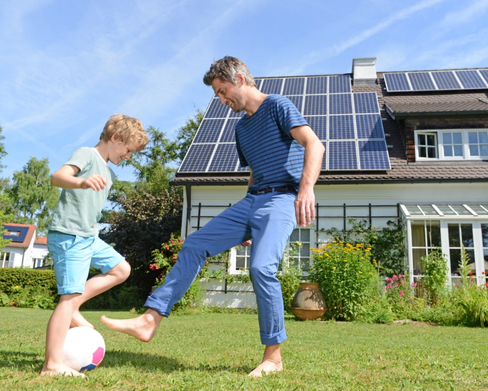 Man and son playing soccer in the front yard of their home with new solar panels