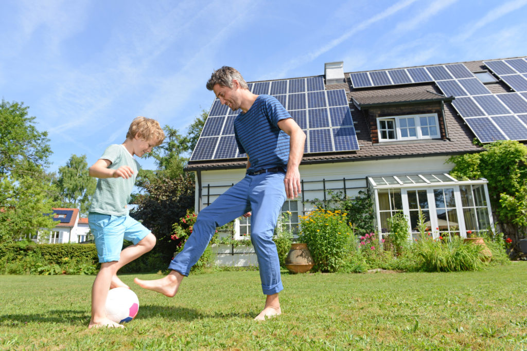 Father and son playing soccer in front yard of home with new rooftop solar panels