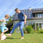 Father and son playing soccer in front yard of home with new rooftop solar panels